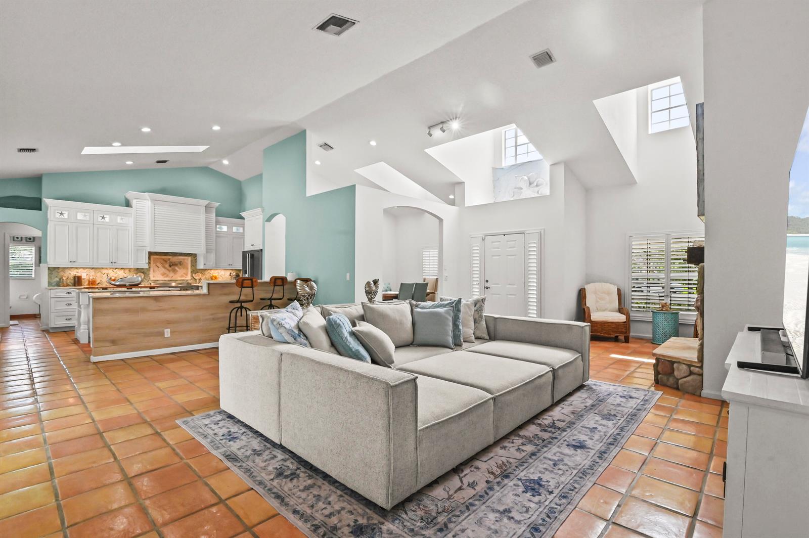 A spacious living room with terracotta tile floors, a large sectional sofa, and kitchen area — 5637 Lago Del Sol Drive, Lake Worth FL 33449, LAKE WORTH, FL
