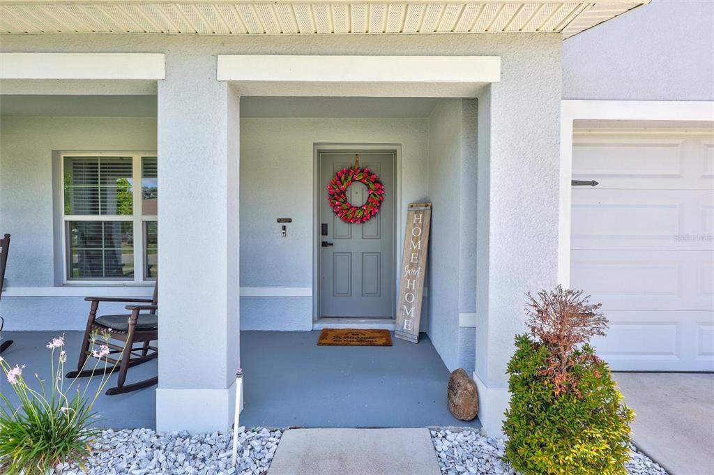 A gray front door with a floral wreath sits under a covered porch — 13878 WINEBERRY DRIVE, DADE CITY, FL