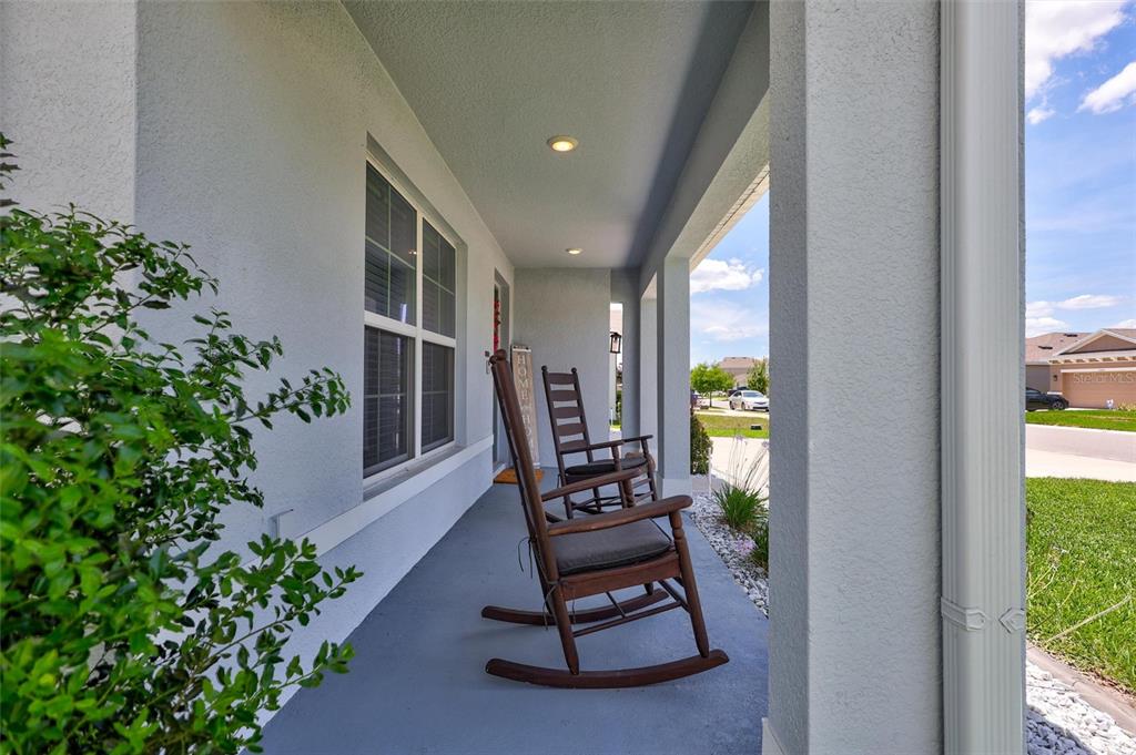 A covered front porch features two wooden rocking chairs and a light gray exterior wall — 13878 WINEBERRY DRIVE, DADE CITY, FL