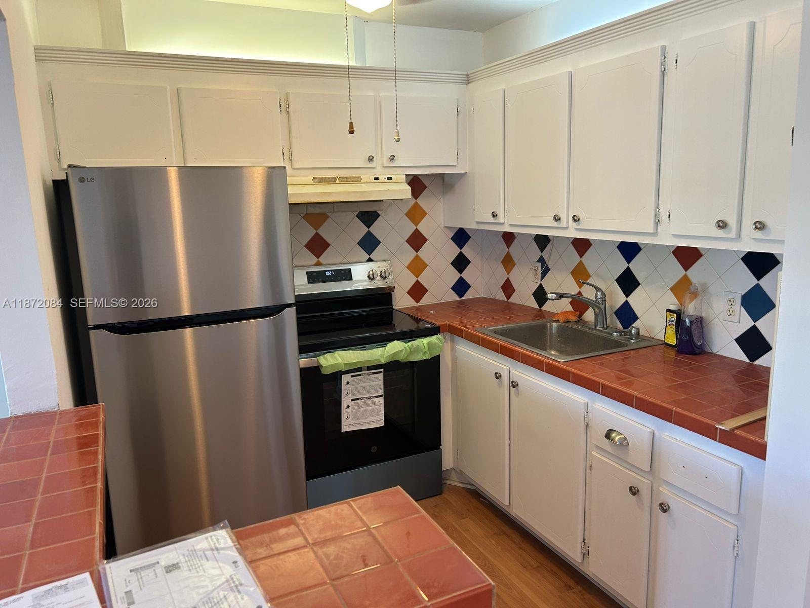 A kitchen features white cabinets, a stainless steel refrigerator, and a colorful diamond-patterned tile backsplash — 19 Newport # A, Deerfield Beach FL 33442, DEERFIELD BEACH, FL