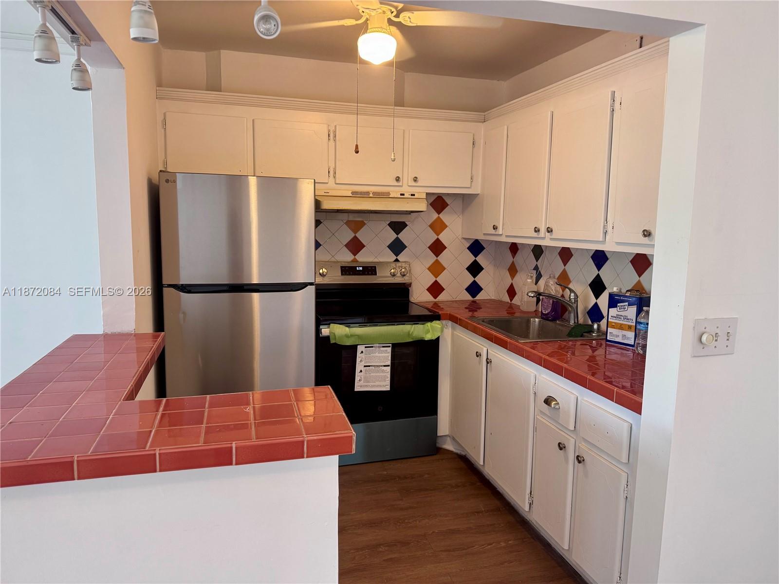 A kitchen features white cabinets, stainless steel appliances, and red tiled countertops and backsplash — 19 Newport # A, Deerfield Beach FL 33442, DEERFIELD BEACH, FL