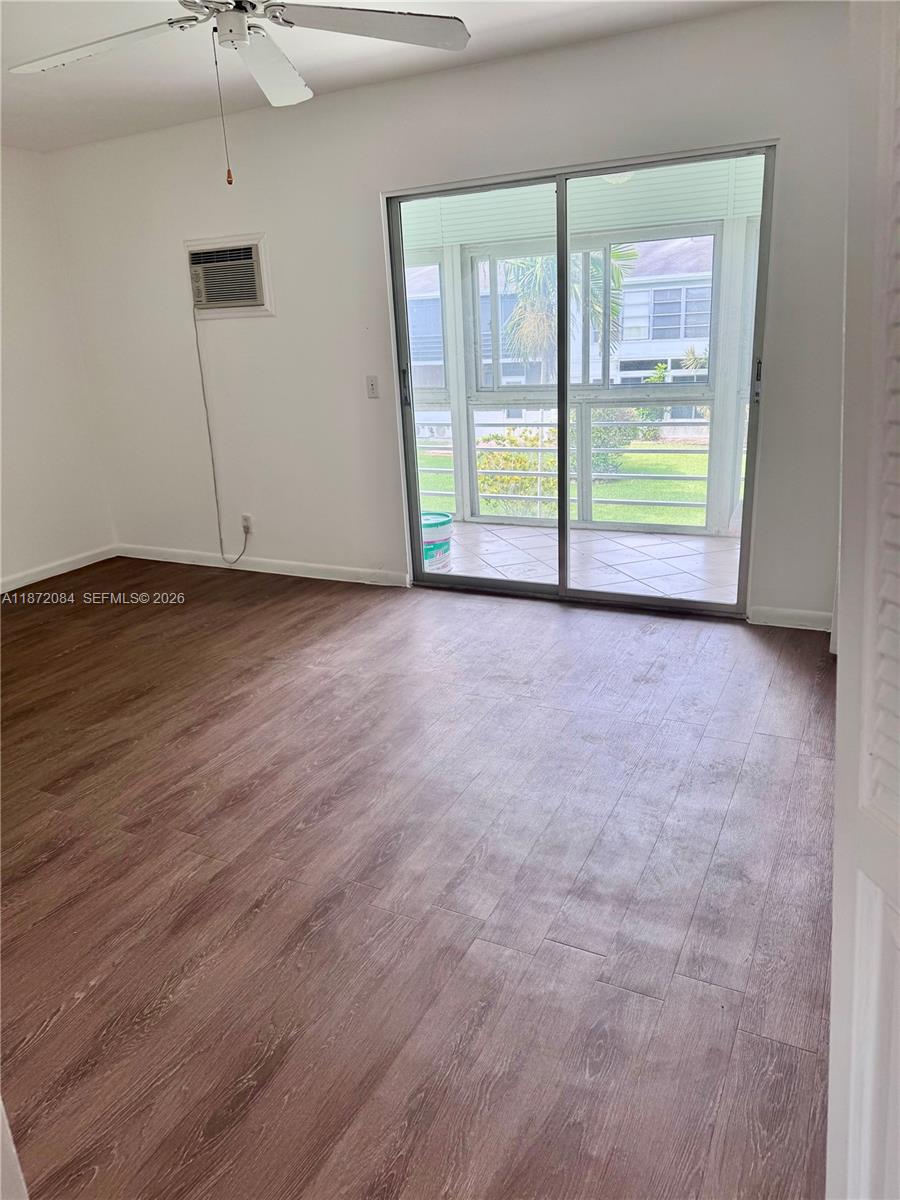 An empty room features wood-look flooring, a ceiling fan, a wall-mounted air conditioner, and sliding doors — 19 Newport # A, Deerfield Beach FL 33442, DEERFIELD BEACH, FL