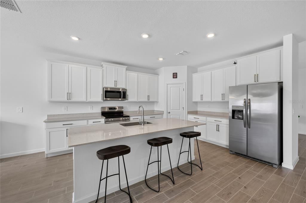 A modern kitchen features white cabinets, stainless steel appliances, a quartz island, and wood-look flooring — 8846 SW 69TH TERRACE, OCALA, FL