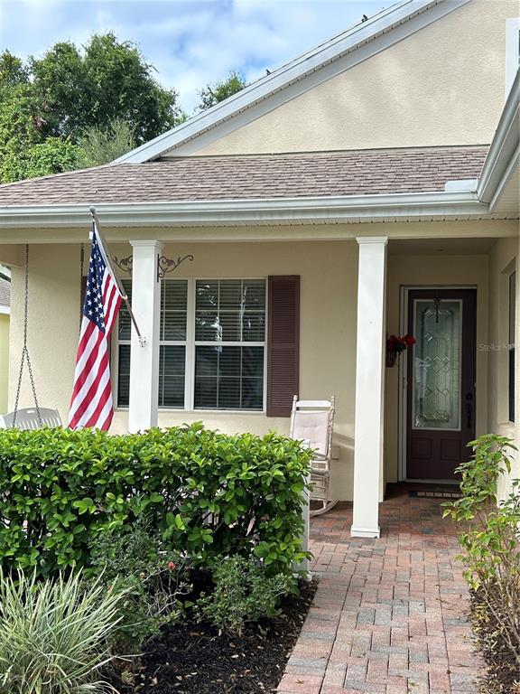 A tan house exterior features a front porch with a rocking chair and American flag — 2205 CALEDONIAN STREET, CLERMONT, FL