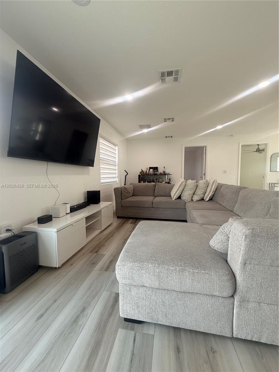 A living room features a large sectional sofa, a wall-mounted television, and light wood-look flooring — 820 N trebol st, Clewiston FL 33440, CLEWISTON, FL