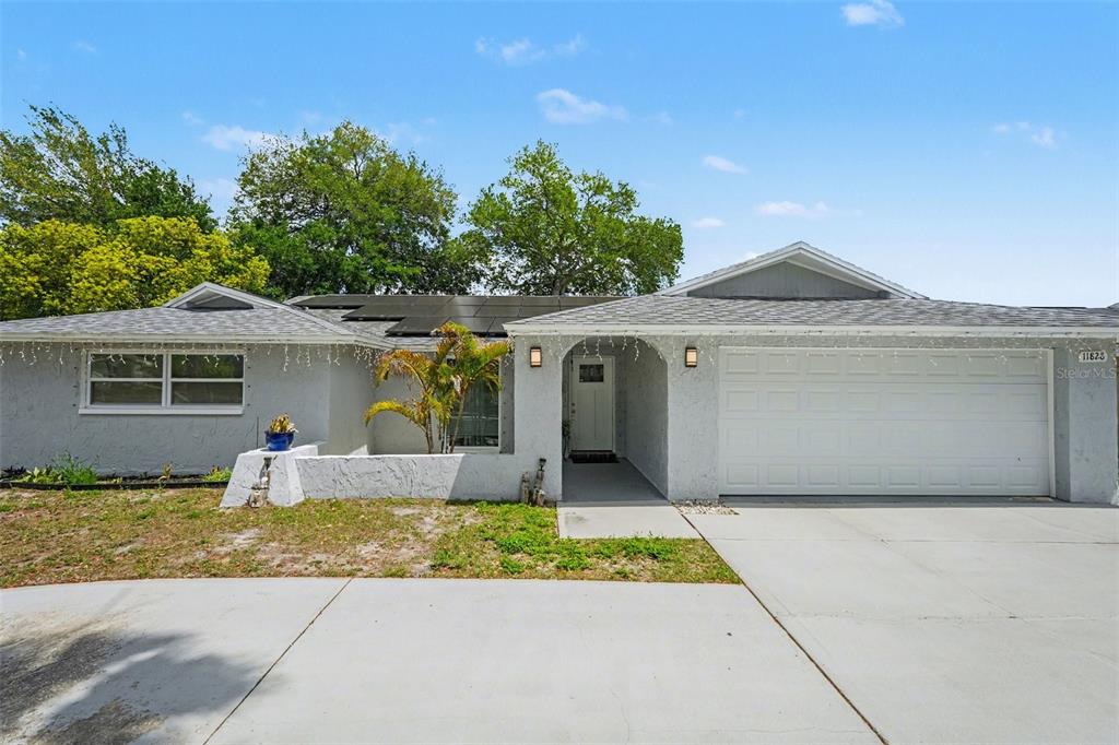A single-story house with a white stucco exterior, a two-car garage, and solar panels — 11828 BINGHAM DRIVE, PORT RICHEY, FL