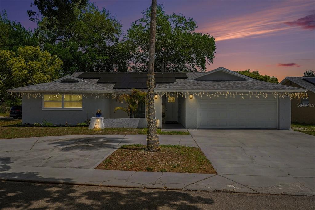 A single-story house with a concrete driveway, solar panels, and string lights at dusk — 11828 BINGHAM DRIVE, PORT RICHEY, FL