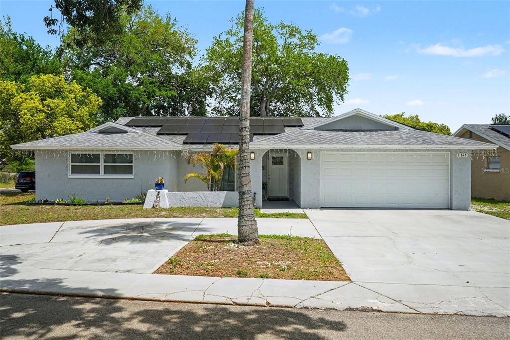A single-story house with a white stucco exterior, a two-car garage, and rooftop solar panels — 11828 BINGHAM DRIVE, PORT RICHEY, FL