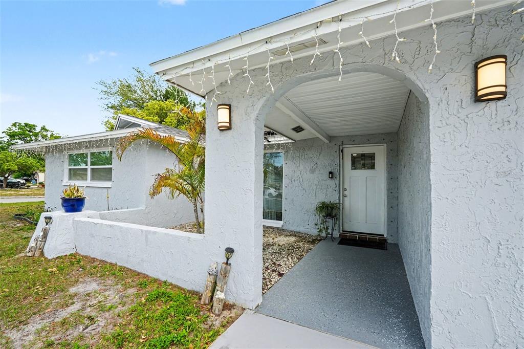 A light gray stucco house exterior features a covered entryway with a white front door — 11828 BINGHAM DRIVE, PORT RICHEY, FL