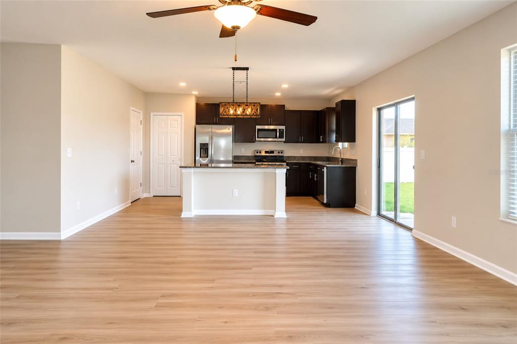 An open-concept kitchen with dark cabinets, stainless steel appliances, and light wood-look flooring — 715 CALICO SCALLOP STREET, RUSKIN, FL