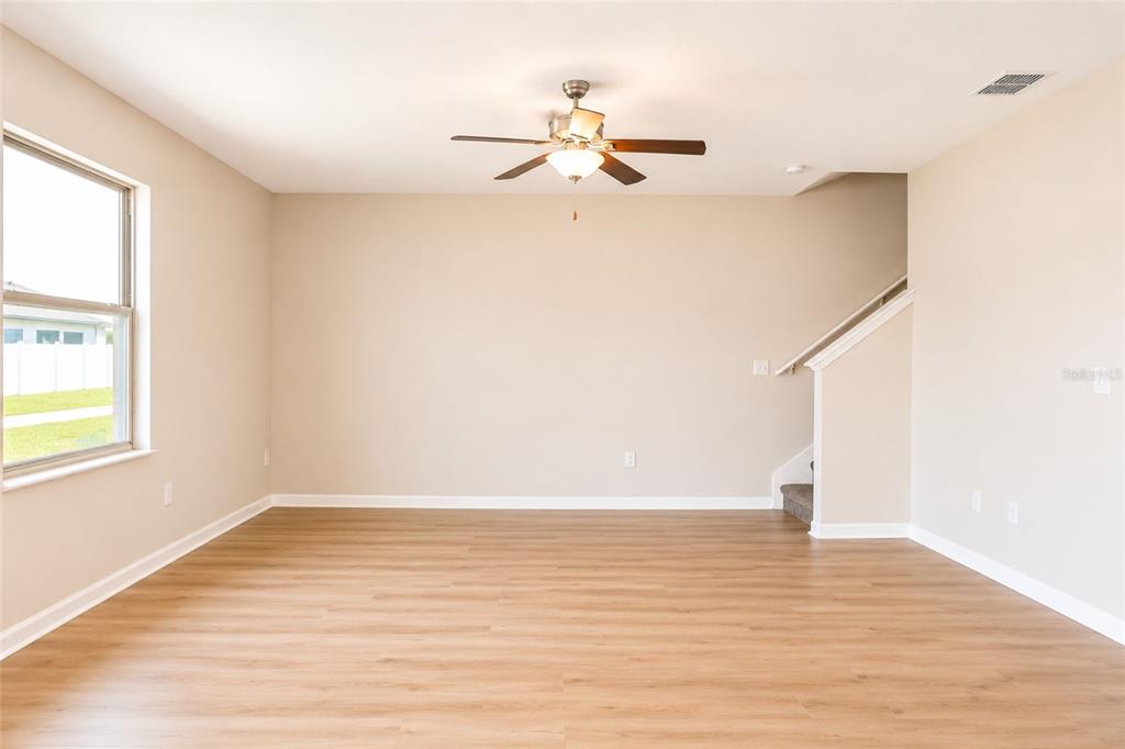An empty living room with light wood-look flooring, a ceiling fan, and a staircase — 715 CALICO SCALLOP STREET, RUSKIN, FL