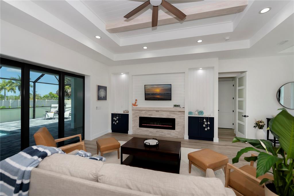 A living room features a tray ceiling, a fireplace with a television, and sliding glass doors — 15384 VISALIA ROAD, PORT CHARLOTTE, FL