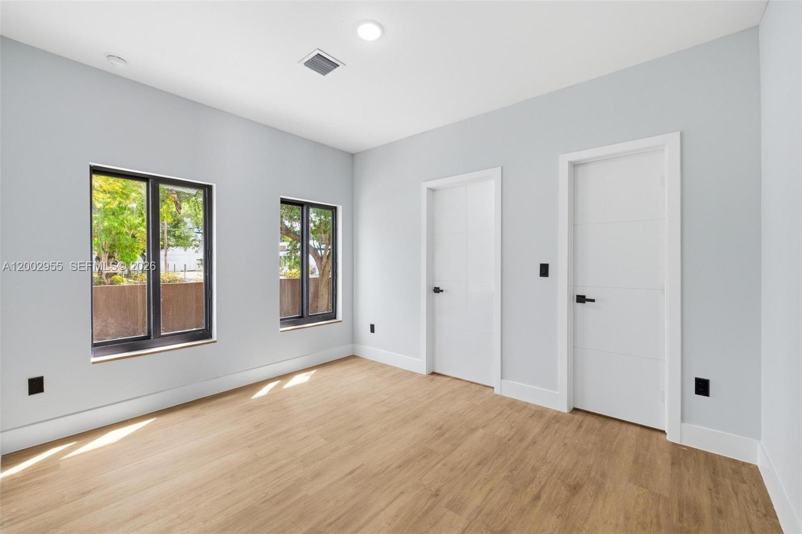 An empty room features light gray walls, wood-look flooring, two windows, and two white doors — 4717 SW 32nd Ave, Dania Beach FL 33312, DANIA BEACH, FL