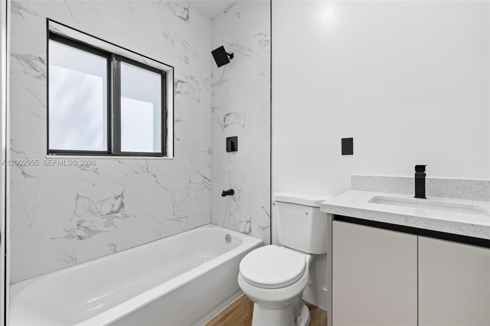 This bathroom features a marble-tiled tub shower, a white toilet, and a modern vanity — 4717 SW 32nd Ave, Dania Beach FL 33312, DANIA BEACH, FL