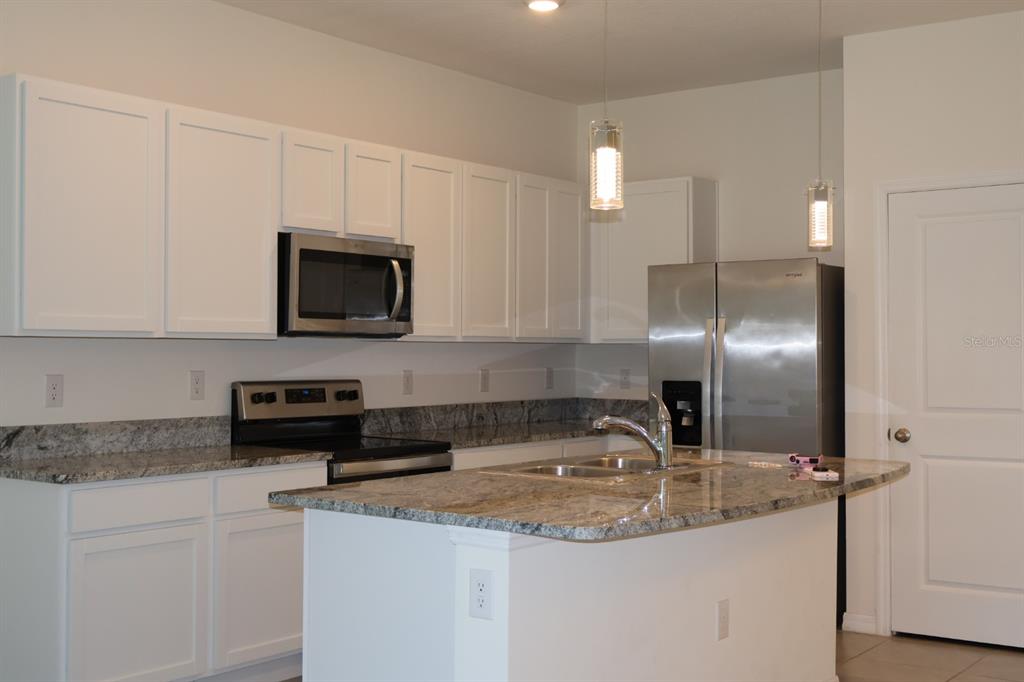 A kitchen features white cabinets, granite countertops, stainless steel appliances, and a central island — 8748 MILESTONE DRIVE, SARASOTA, FL