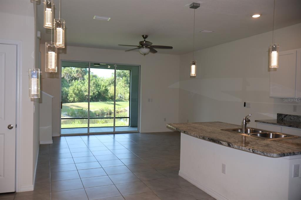 A kitchen with granite countertops and a pendant light overlooks a living area with tile — 8748 MILESTONE DRIVE, SARASOTA, FL
