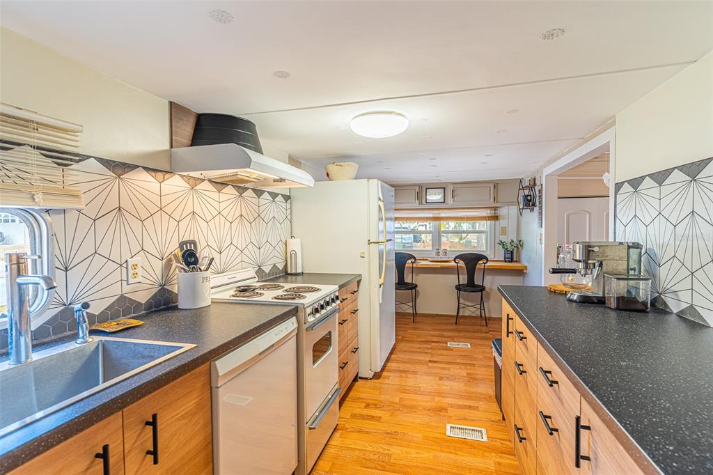 A kitchen features wood cabinets, black countertops, a geometric tile backsplash, and stainless appliances — 77 SILVERSIDES STREET, LAKE WALES, FL