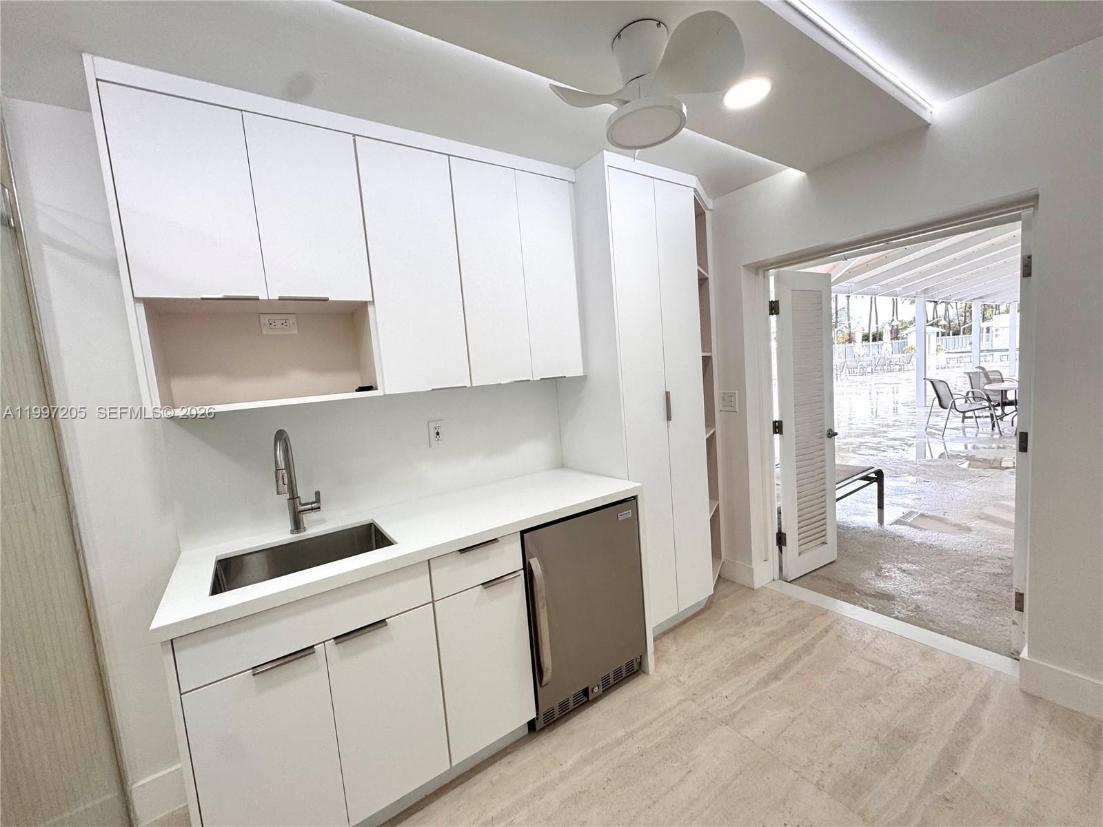 A white kitchenette with a sink and under-counter refrigerator opens to a covered patio — 2899 Collins Ave # 6, Miami Beach FL 33140, MIAMI BEACH, FL