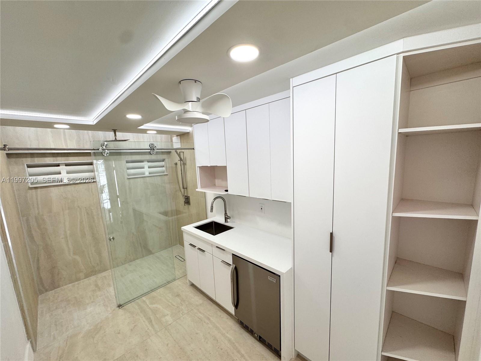 A modern kitchenette with white cabinetry and a small refrigerator sits beside a glass-enclosed shower — 2899 Collins Ave # 6, Miami Beach FL 33140, MIAMI BEACH, FL
