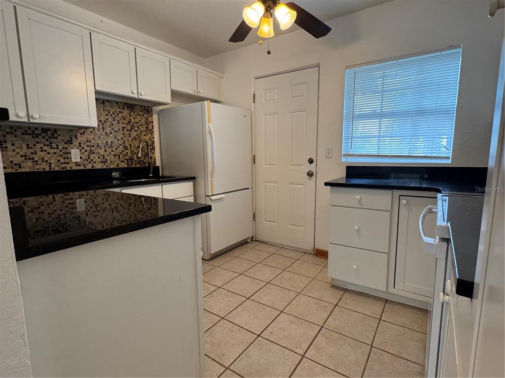 A kitchen features white cabinets, black countertops, a mosaic tile backsplash, and tile flooring — 4418 ELI STREET, ORLANDO, FL