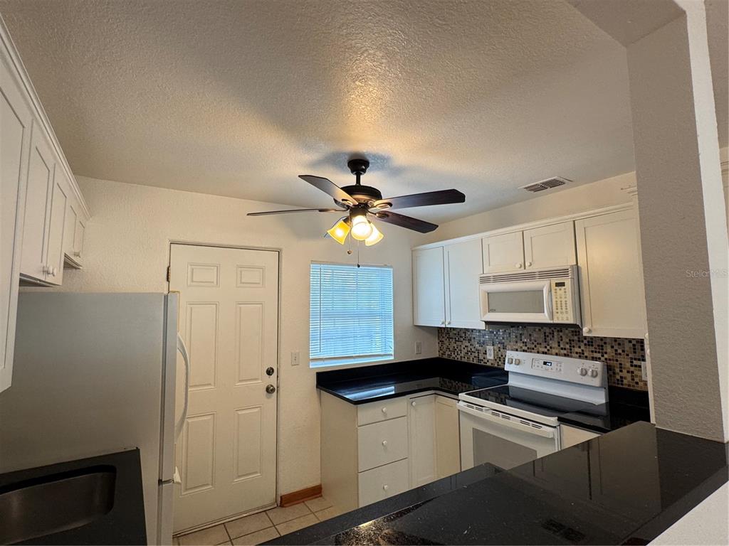 A kitchen features white cabinets, black countertops, a ceiling fan, and a white refrigerator — 4418 ELI STREET, ORLANDO, FL