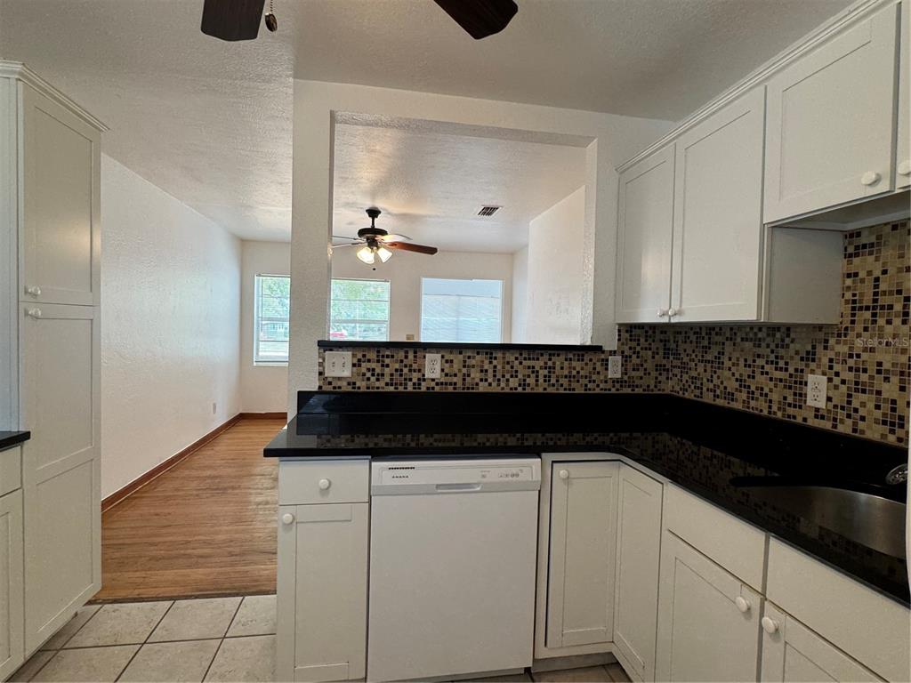 A kitchen with white cabinets, black countertops, and a mosaic tile backsplash overlooks a living area — 4418 ELI STREET, ORLANDO, FL