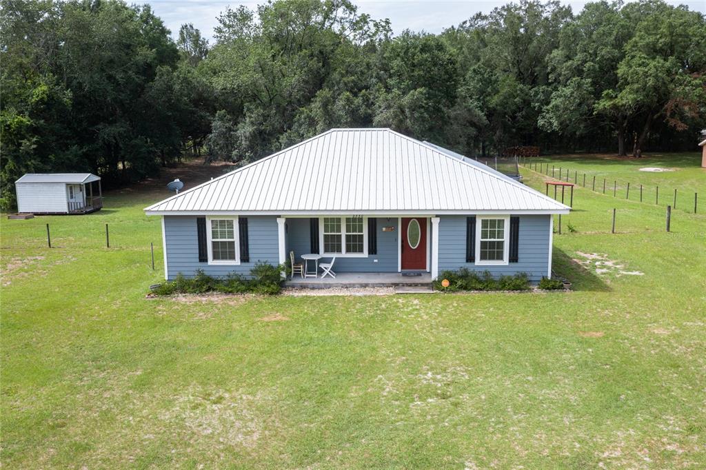 A blue single-story house with a white metal roof sits on a large grassy lot — 2830 NW 174 STREET, TRENTON, FL