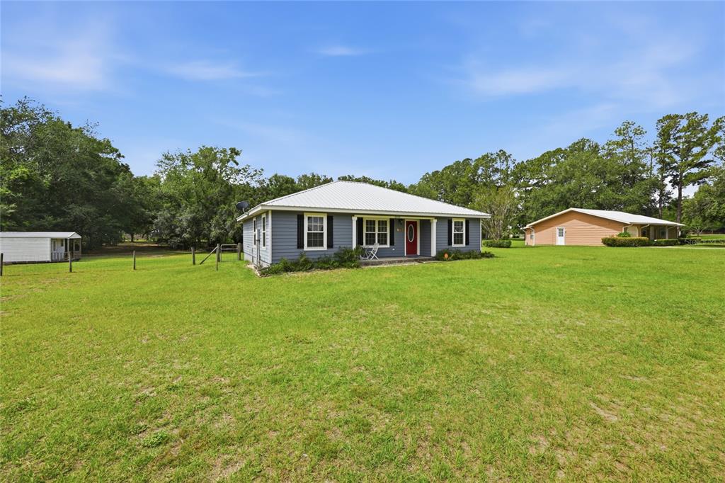 A blue, single-story house with a metal roof sits on a large, grassy lot — 2830 NW 174 STREET, TRENTON, FL