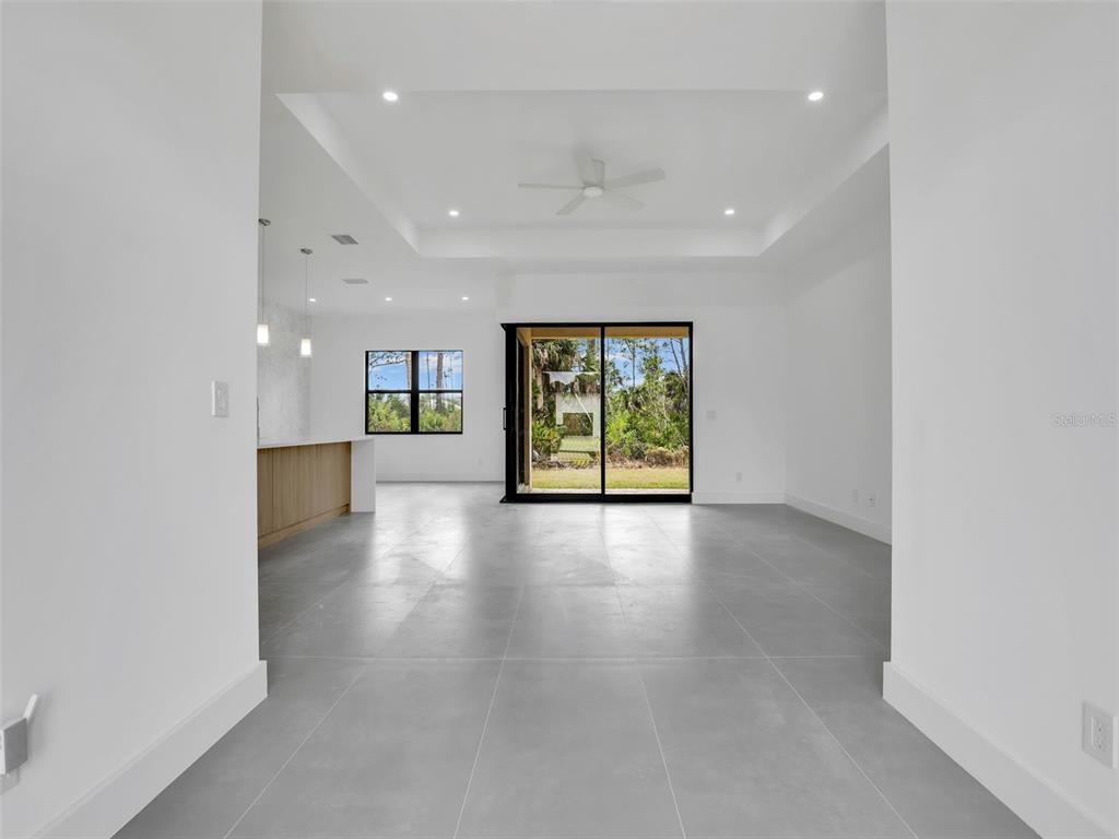 An open-concept living area features gray tile flooring, a tray ceiling, and sliding glass doors — 11161 CARNEGIE AVENUE, ENGLEWOOD, FL