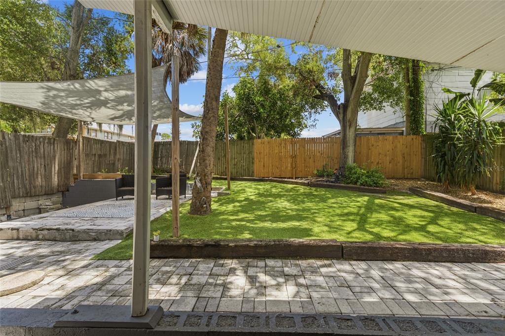 A backyard features a paved patio, artificial turf lawn, wooden fencing, and a shade sail — 1413 N OSCEOLA AVENUE, CLEARWATER, FL