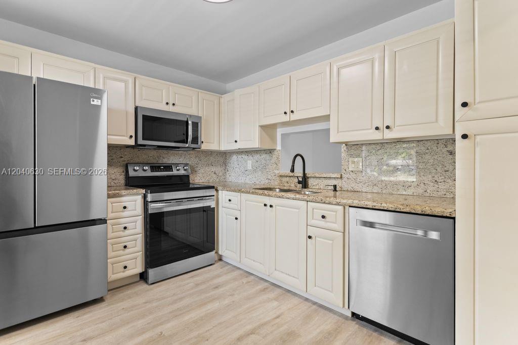 A kitchen features cream-colored cabinets, stainless steel appliances, and speckled granite countertops — 414 SE 10th St # 108, Dania Beach FL 33004, DANIA BEACH, FL