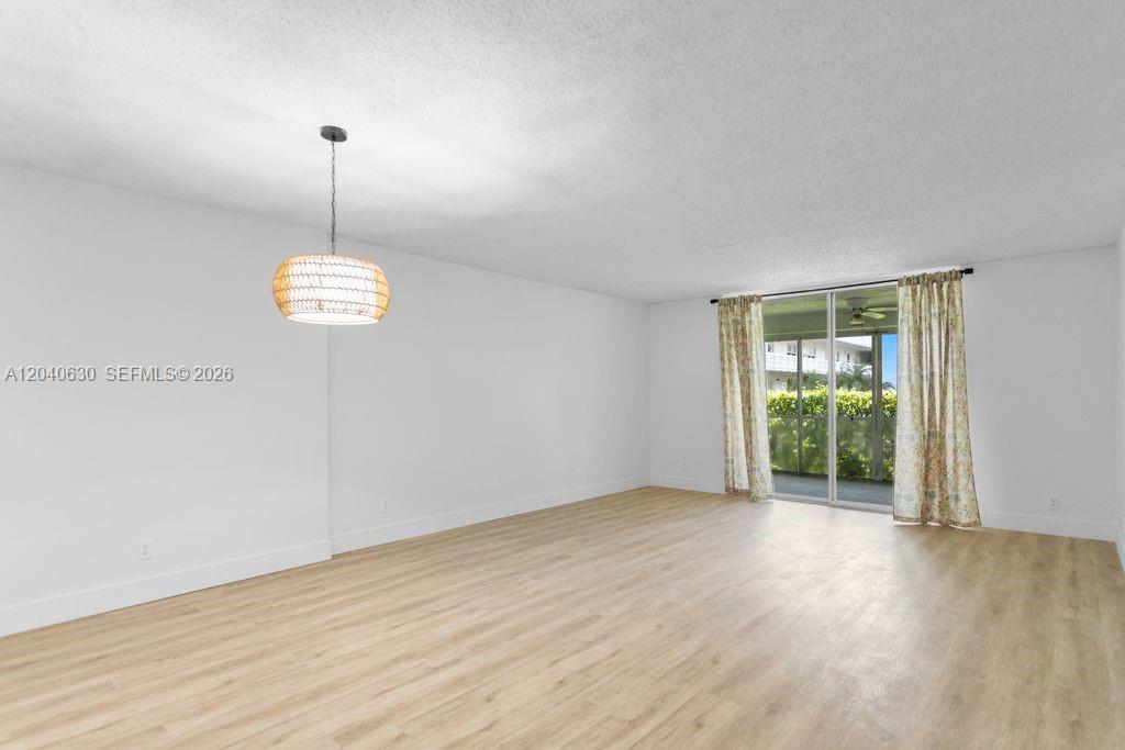 An empty room features light wood-look flooring, white walls, a woven pendant light, and sliding doors — 414 SE 10th St # 108, Dania Beach FL 33004, DANIA BEACH, FL