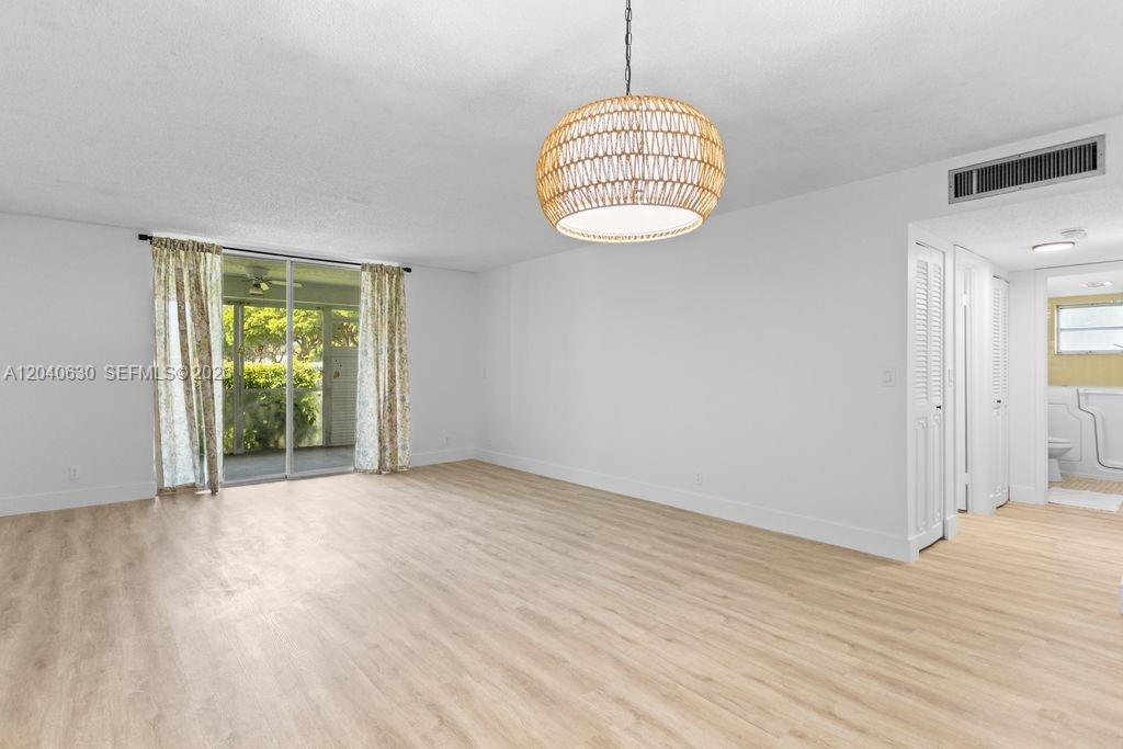 A bright, empty room features light wood-look flooring, white walls, and a woven pendant light — 414 SE 10th St # 108, Dania Beach FL 33004, DANIA BEACH, FL