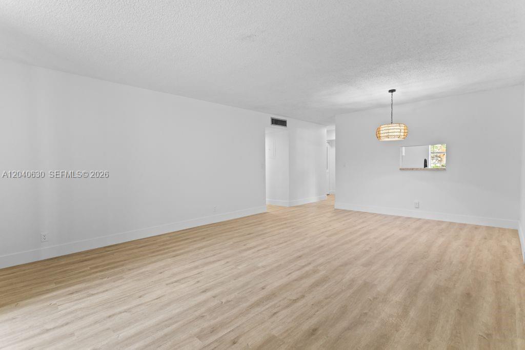 An empty room features light wood-look flooring, white walls, and a hanging woven light fixture — 414 SE 10th St # 108, Dania Beach FL 33004, DANIA BEACH, FL