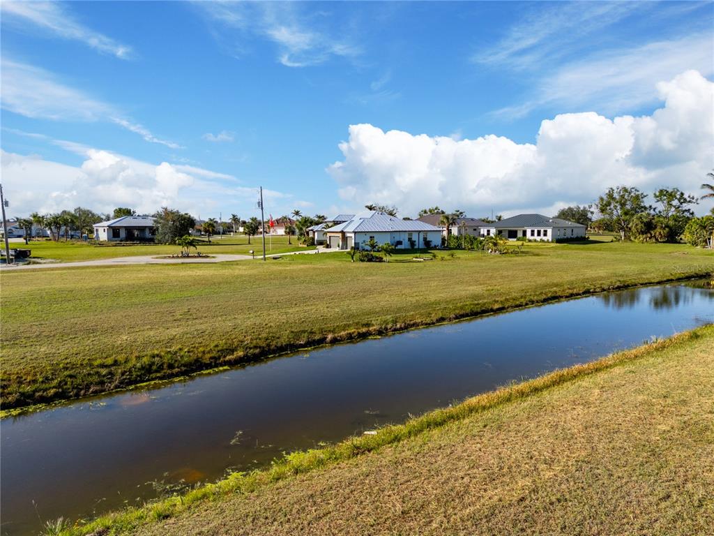 A canal runs through a grassy field in front of several suburban houses — 17277 CAPE HORN BOULEVARD, PUNTA GORDA, FL