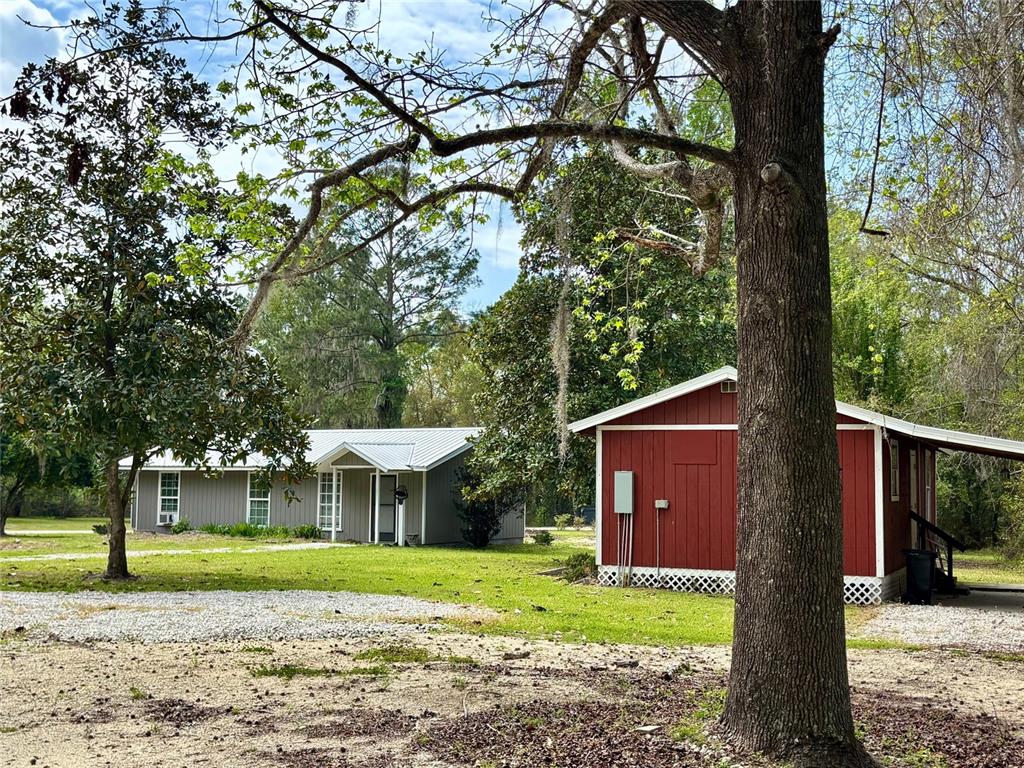 A gray house and a red shed sit on a grassy lot with large trees — 18917 NW COUNTY ROAD 239, ALACHUA, FL