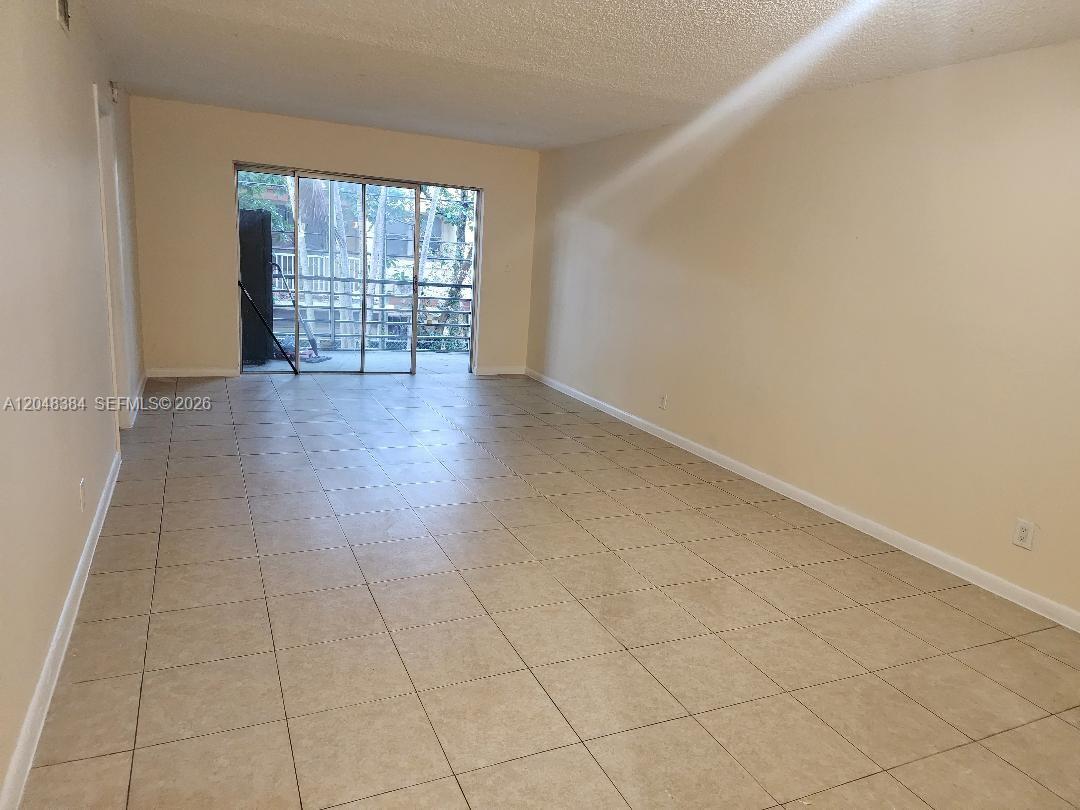 An empty room features beige tile flooring, light-colored walls, and a sliding glass balcony door — 1700 NW 58th Ter # 2E, Sunrise FL 33313, SUNRISE, FL