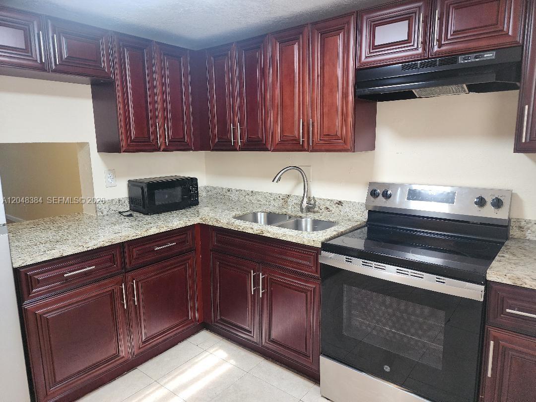 A kitchen features dark wood cabinets, granite countertops, and stainless steel appliances — 1700 NW 58th Ter # 2E, Sunrise FL 33313, SUNRISE, FL
