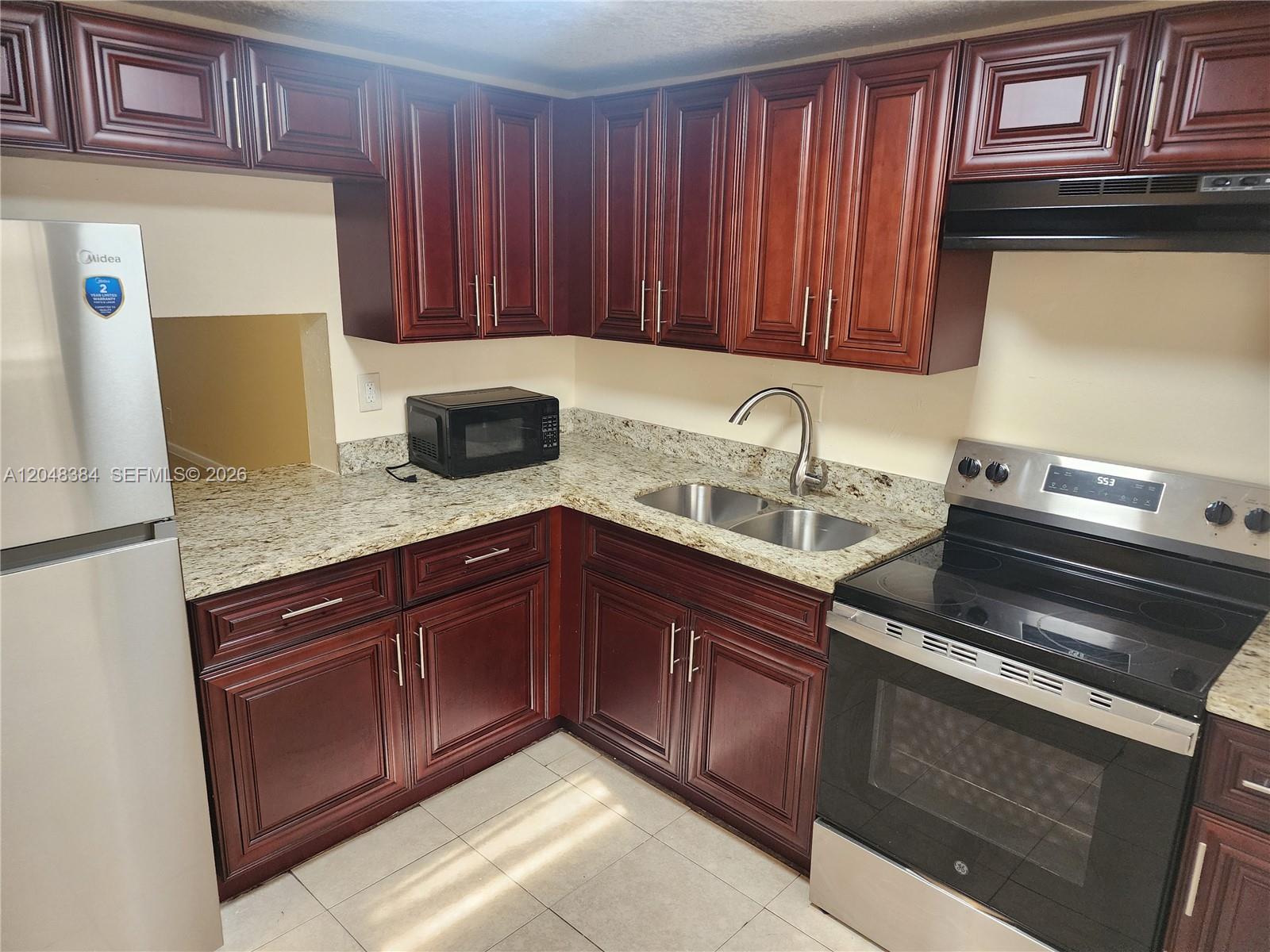 A kitchen features dark wood cabinets, granite countertops, stainless steel appliances, and tile flooring — 1700 NW 58th Ter # 2E, Sunrise FL 33313, SUNRISE, FL