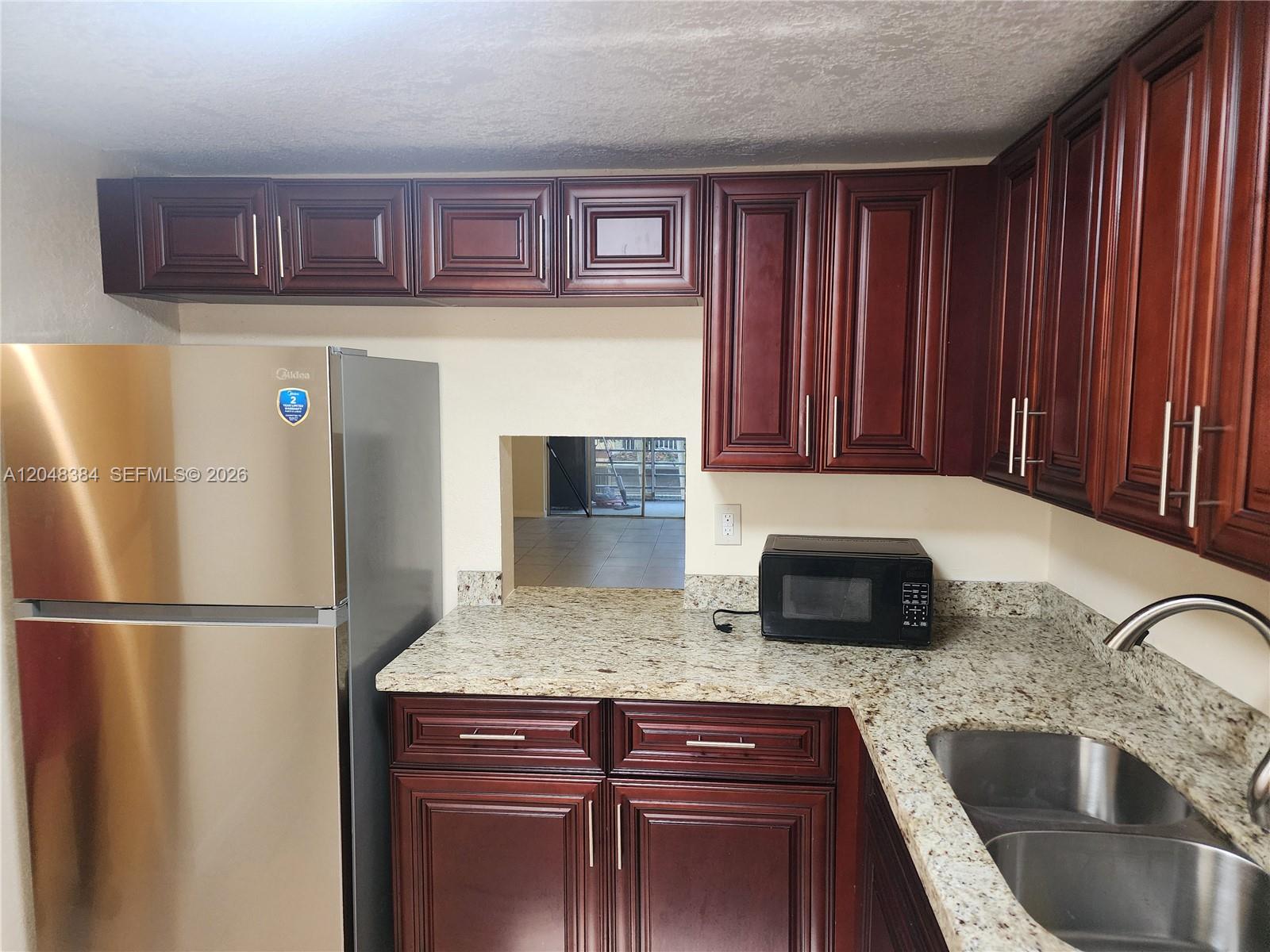 A kitchen features dark wood cabinets, granite countertops, a stainless steel refrigerator, and a pass-through window — 1700 NW 58th Ter # 2E, Sunrise FL 33313, SUNRISE, FL