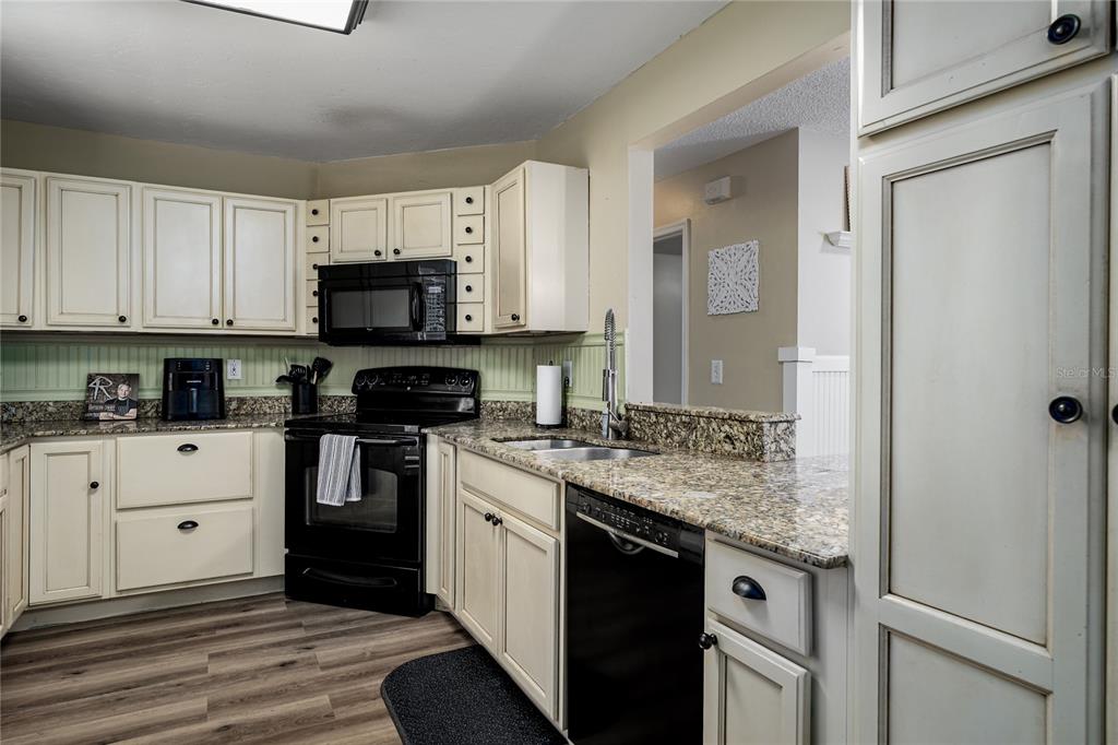 A kitchen features off-white cabinets, granite countertops, black appliances, and wood-look flooring — 3320 5TH DRIVE W, PALMETTO, FL