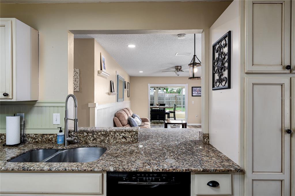 A kitchen sink and granite countertop look through a pass-through window into a living area — 3320 5TH DRIVE W, PALMETTO, FL
