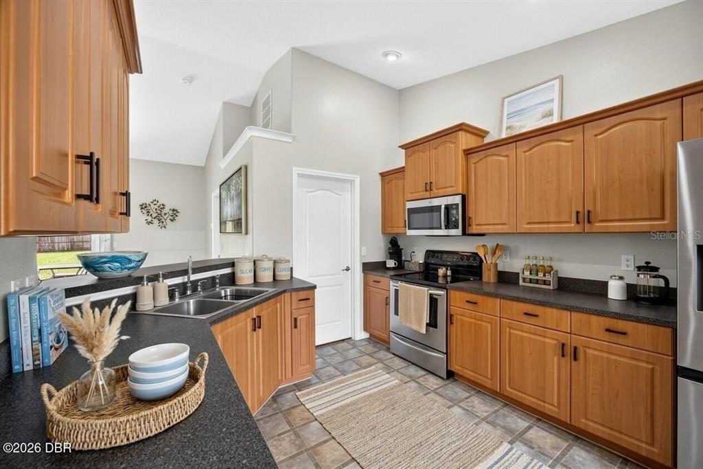 A kitchen features wood cabinets, dark countertops, stainless steel appliances, and a tiled floor — 1901 EDEN DRIVE, DELTONA, FL