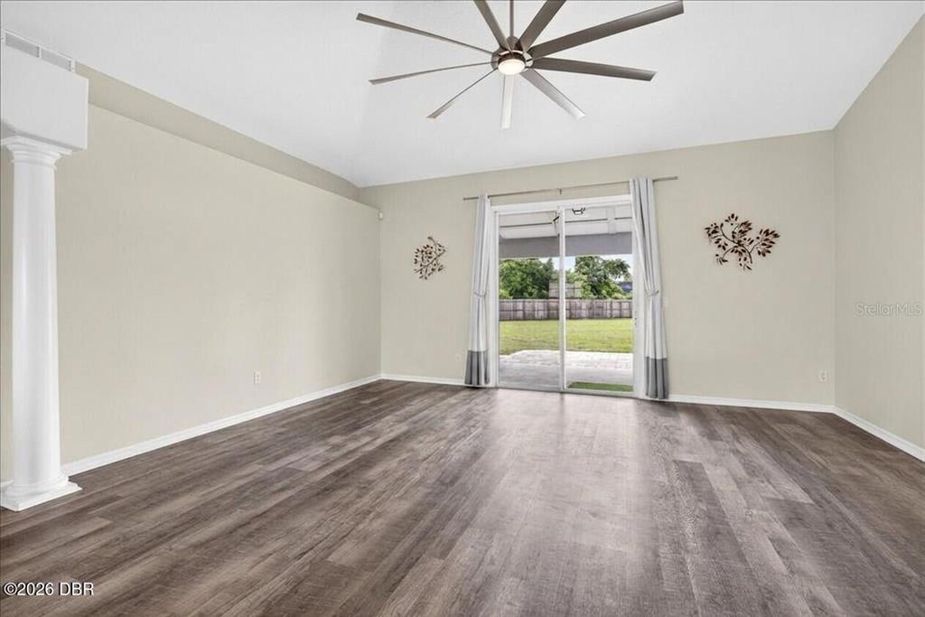 An empty room features wood-look flooring, a ceiling fan, a white pillar, and sliding glass doors — 1901 EDEN DRIVE, DELTONA, FL