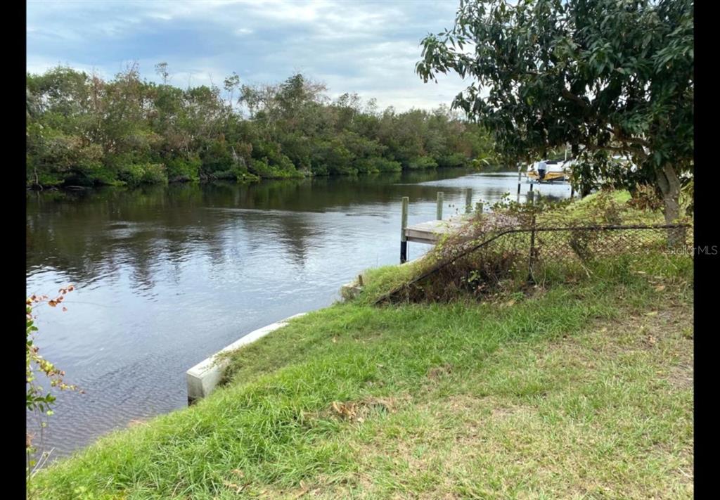 A grassy backyard slopes down to a canal with a small wooden dock and boat — 4150 GARDNER DRIVE, PORT CHARLOTTE, FL