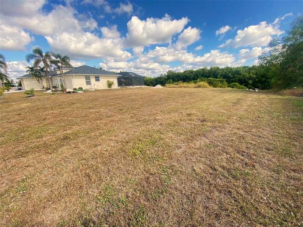 A large, dry, grassy lot sits next to a single-story house with a pool enclosure — 4150 GARDNER DRIVE, PORT CHARLOTTE, FL