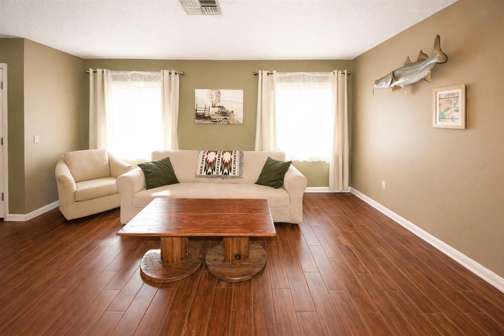 A living room features a beige sofa, an armchair, a wooden spool coffee table, and wood-look flooring — 13277 DELBARTON STREET, SPRING HILL, FL