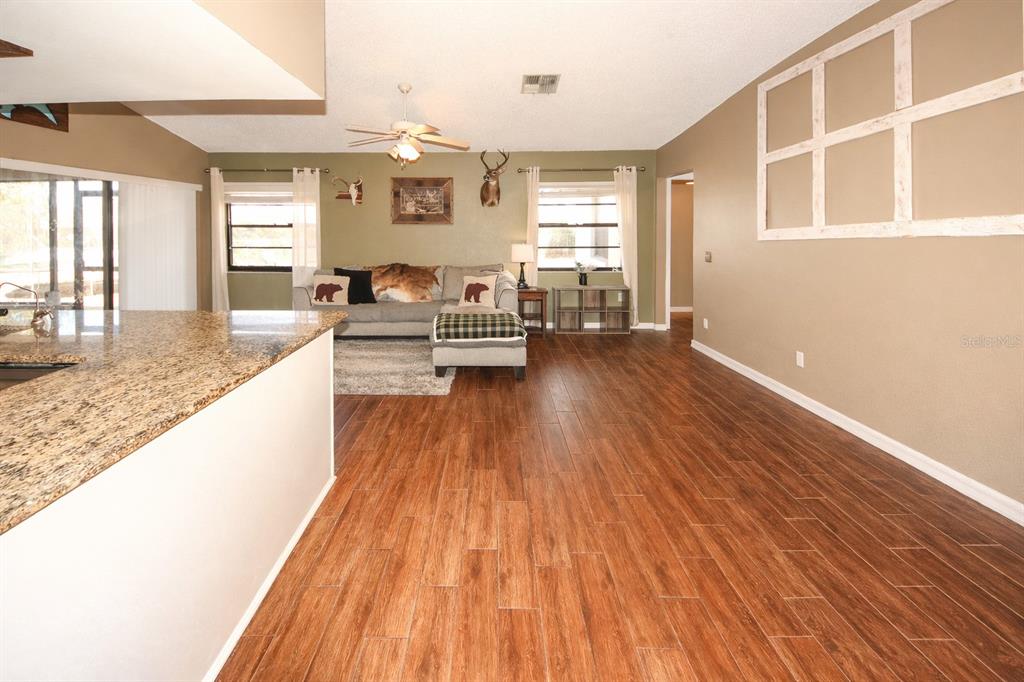 A living room with wood-look tile flooring, a granite-topped kitchen island, and a gray sofa — 13277 DELBARTON STREET, SPRING HILL, FL