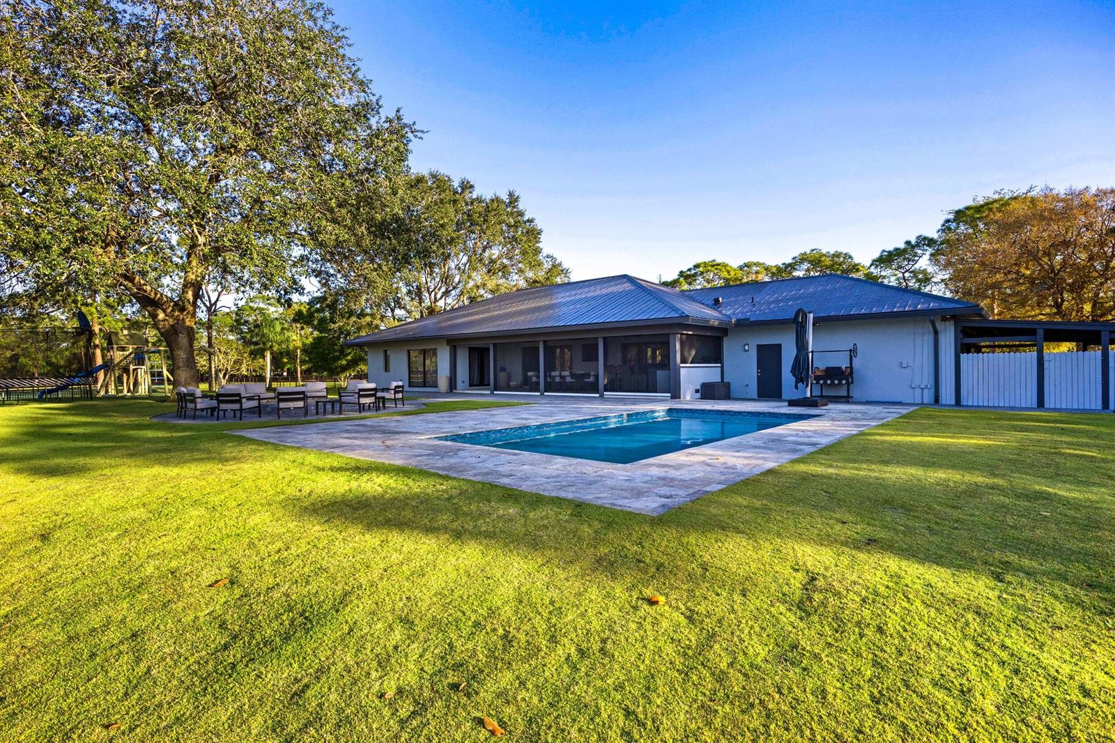 A backyard features a rectangular swimming pool, a stone patio, and a house with metal roofing — 20000 SE Mack Dairy Road SE, Jupiter FL 33478, JUPITER, FL