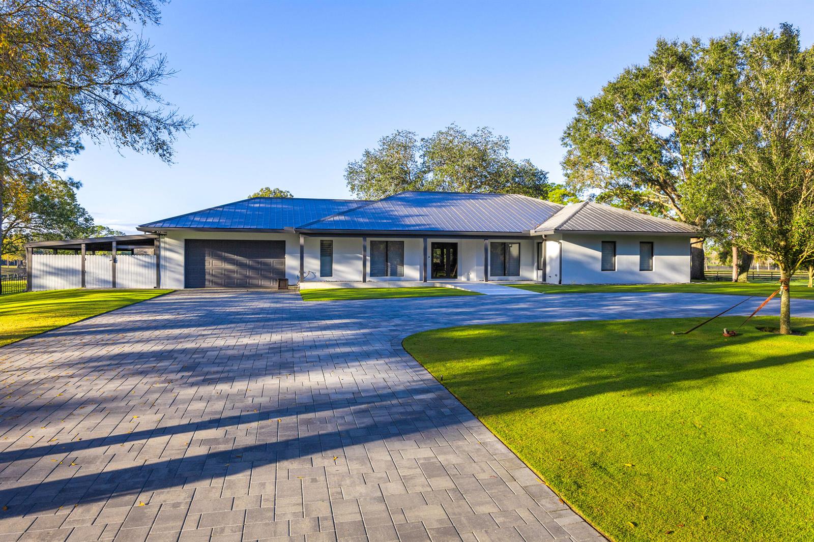 A single-story house with a metal roof, gray exterior, and a large paved driveway — 20000 SE Mack Dairy Road SE, Jupiter FL 33478, JUPITER, FL